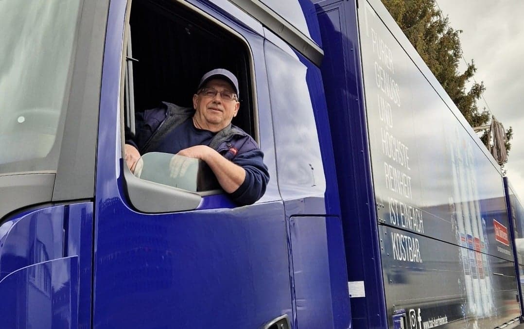 Ein%20Lastwagenfahrer%20mit%20blauer%20Kappe%20und%20dunkler%20Jacke%20l%E4chelt%20aus%20dem%20Fenster%20seines%20blauen%20Lieferwagens%2C%20auf%20dessen%20Seite%20das%20%22Bad%20D%FCrrheimer%22-Logo%20und%20der%20Slogan%20zu%20sehen%20sind.